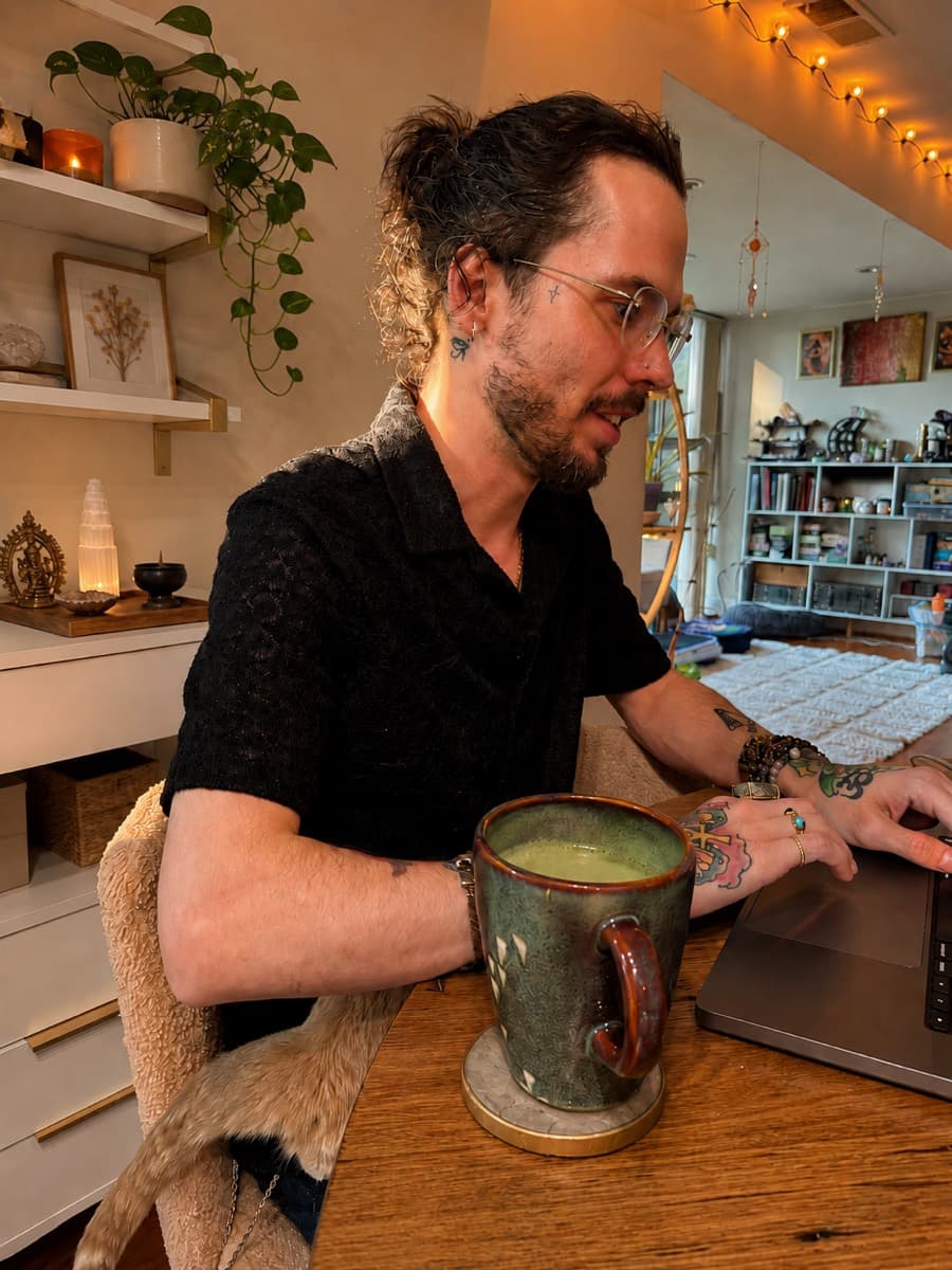 Adam working at his desk with a matcha, plants and crystals around the room